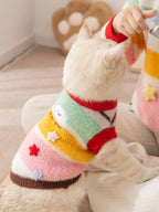 A person holds a cat wearing a colorful striped knit sweater, showing the side of the garment.
