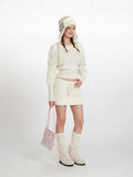 Woman in a white knit sweater and skirt set, holding a pink handbag and wearing a knit hat.
