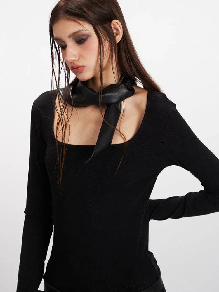 Detailed view of the black long-sleeve ribbed top with a square neckline and a black scarf tied around the neck.