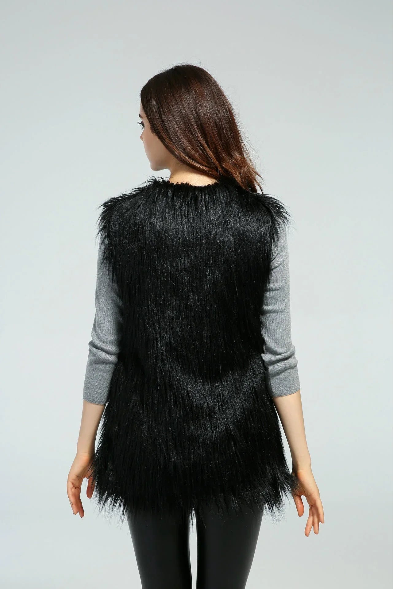 Woman wearing a black faux fur vest over a grey long-sleeved shirt, back view