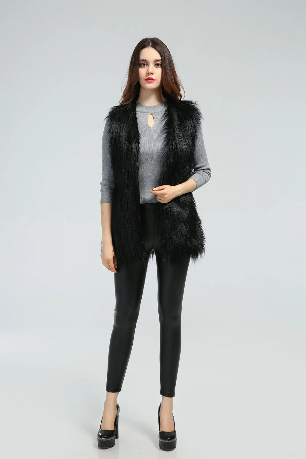 Woman wearing a black faux fur vest over a grey long-sleeved shirt and black pants, front view