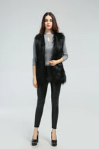 Woman wearing a black faux fur vest over a grey long-sleeved shirt and black pants, front view