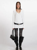 Model wearing a white long-sleeve V-neck top with a black belt and dark wash jeans.