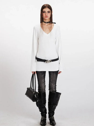 Model wearing a white long-sleeve V-neck top with a black belt and dark wash jeans.