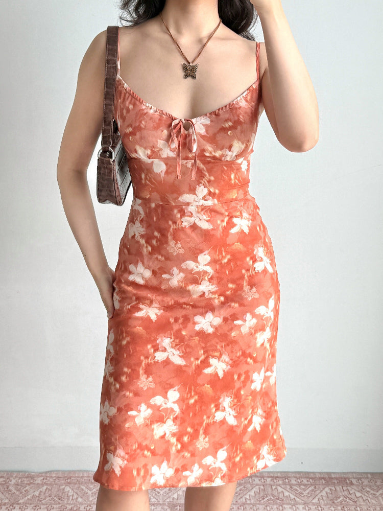 Rear view of a woman in an orange floral print midi dress with spaghetti straps.