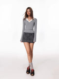 Full body shot of a woman in a grey long-sleeve top with a white collar, grey socks, and black and red sneakers.