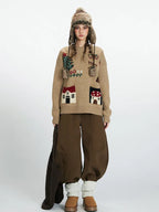 Woman wearing a tan knit sweater with house appliqués and a winter hat