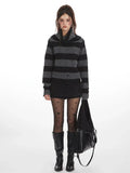 Woman wearing a grey and black striped knit sweater with a cowl neck, black shorts, black patterned tights, and black boots, holding a black handbag.