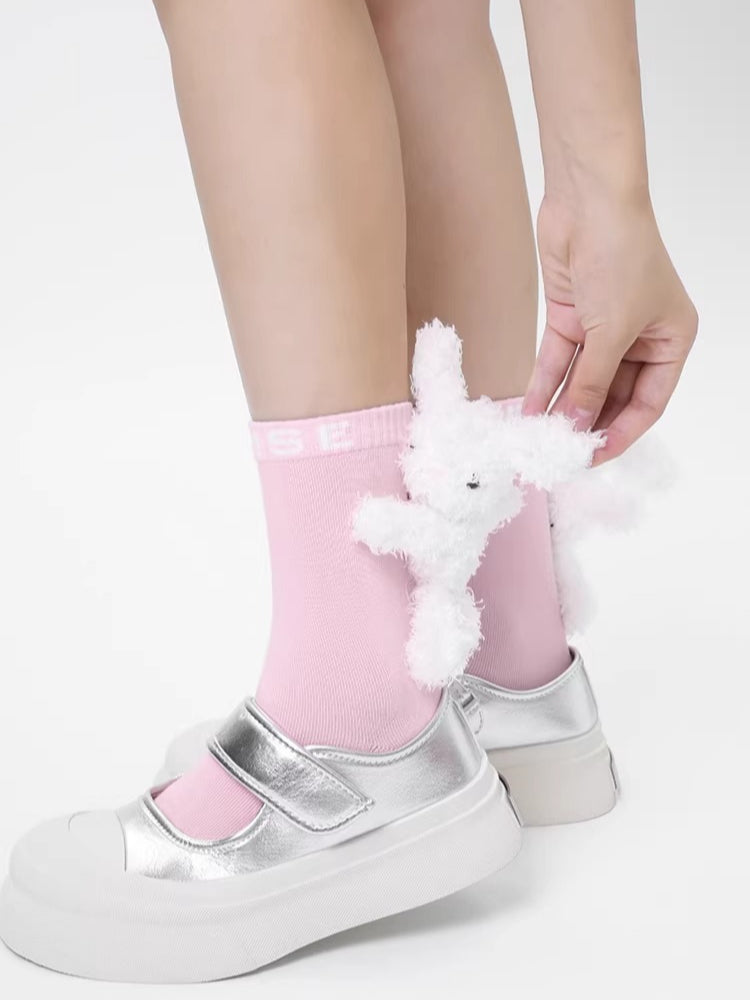 A hand adjusting a plush white bunny charm on a pink crew sock with an 'MSE' logo.