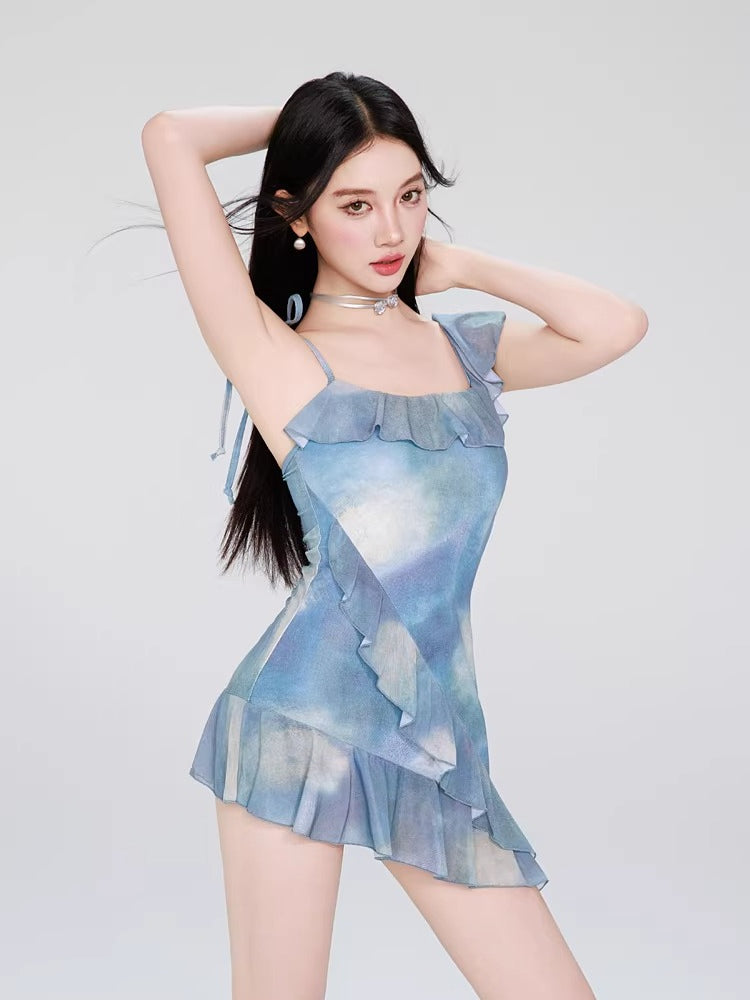 Woman posing with arms raised wearing a blue tie-dye mini dress with ruffle trim and square neckline