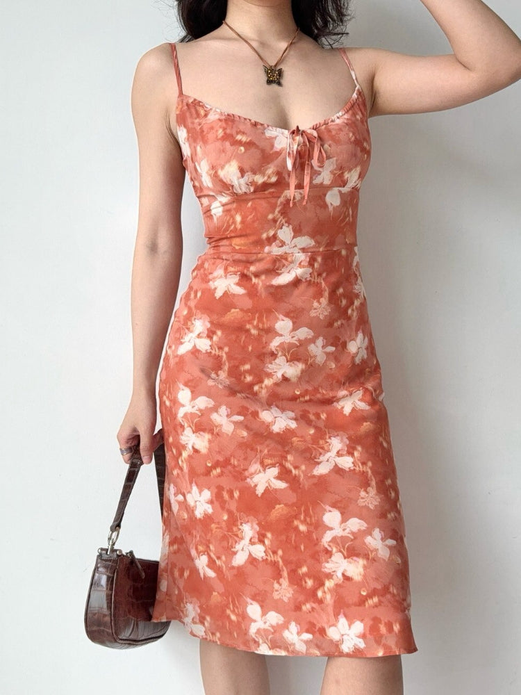 Woman wearing an orange floral print midi dress with spaghetti straps and a tie front detail.