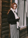Woman adjusting a cream scarf while wearing a black sweater and grey pants.