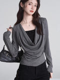 Woman holding black handbag with grey draped cowl neck long sleeve top