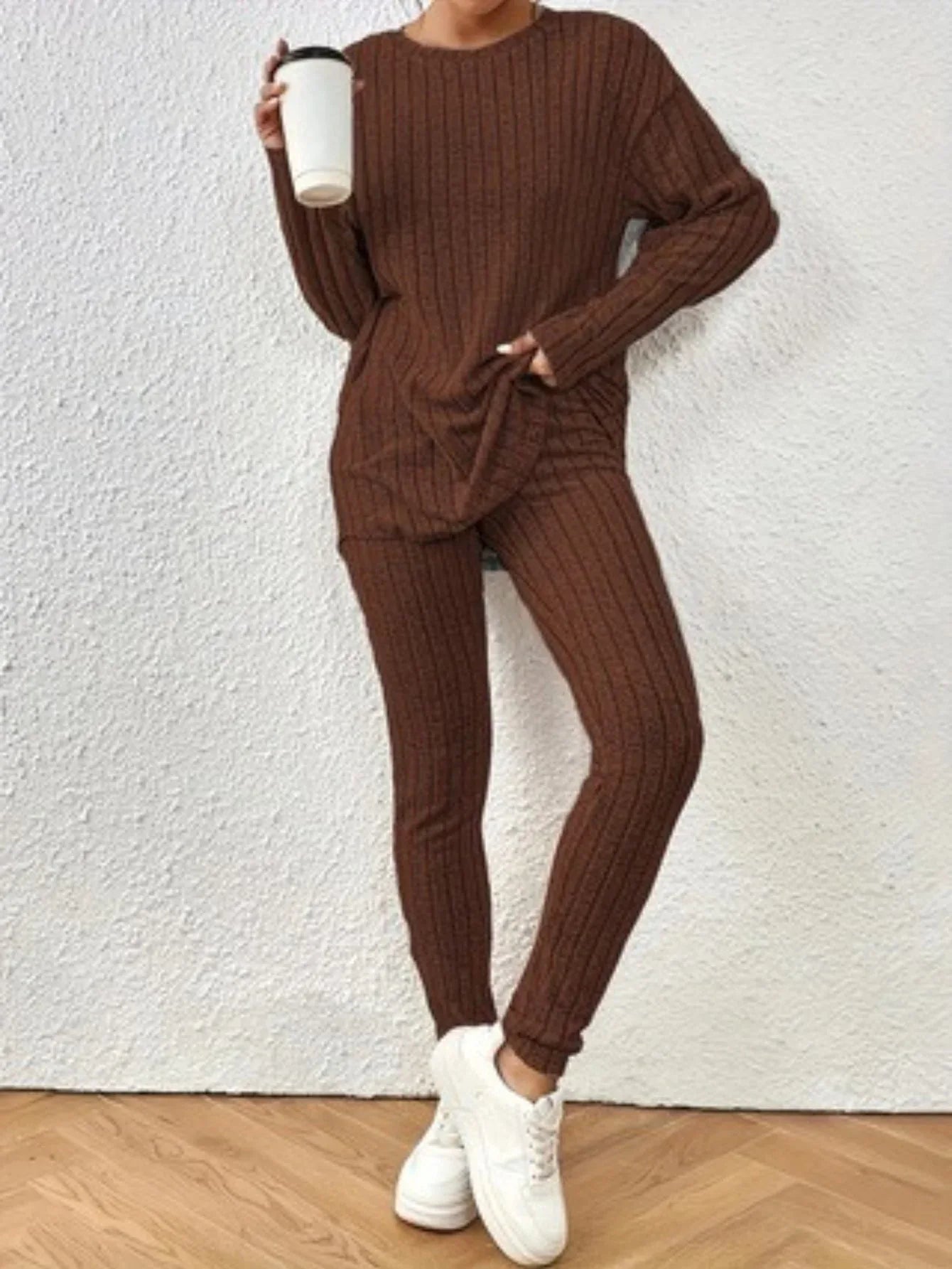 Woman holding a white cup while wearing a brown ribbed knit loungewear set with a crew neck top and slim-fit pants.