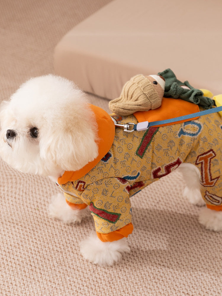 Side profile of a small white dog wearing a yellow patterned dog jacket with orange trim and a leash attached.