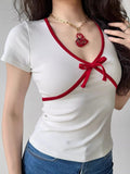 Close-up of a white ribbed knit top with red V-neck trim and a tied bow