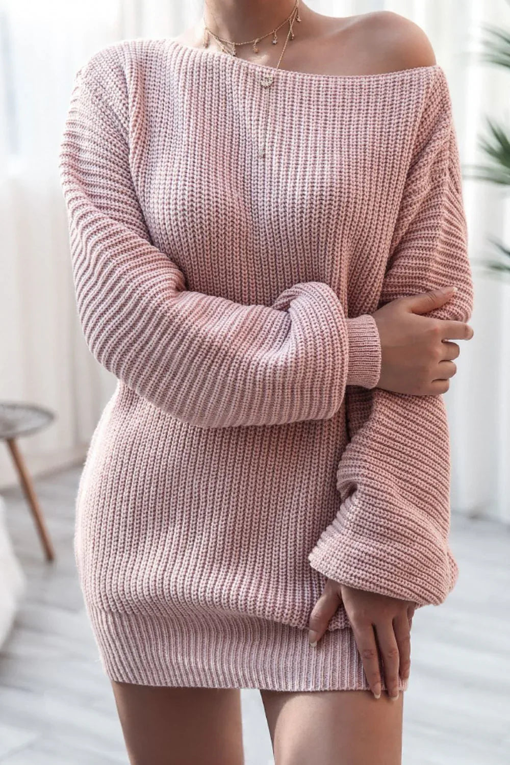 Model posing in a pink off-the-shoulder knit tunic sweater