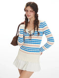 Woman posing with a brown handbag and a blue and white striped sweater.