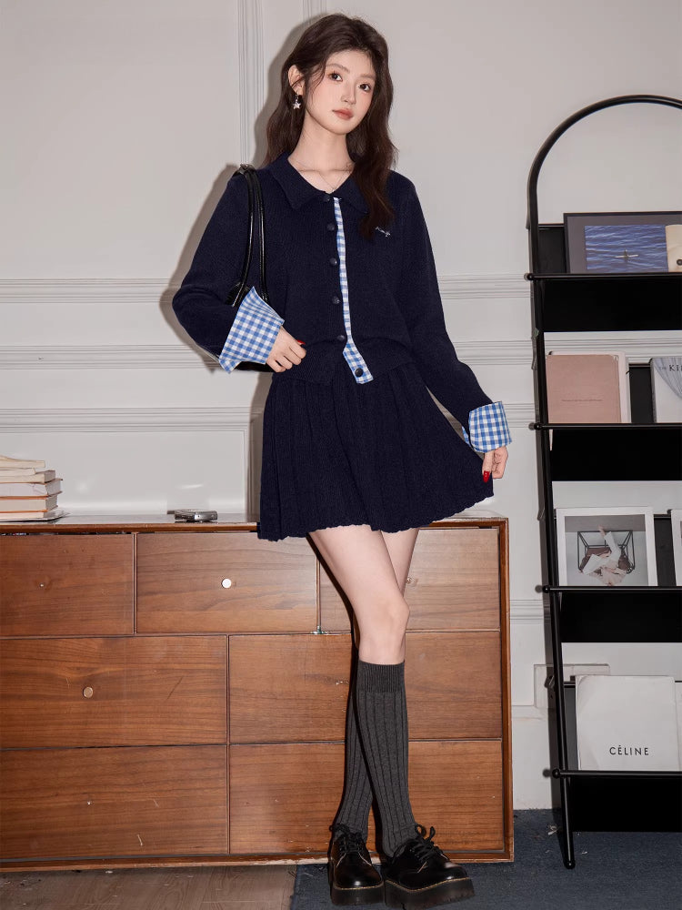 Woman in a navy knit cardigan and pleated skirt, accessorized with a black handbag and dark platform shoes.