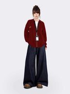 Full body shot of a woman wearing a red collared knit jacket and wide-leg denim pants.