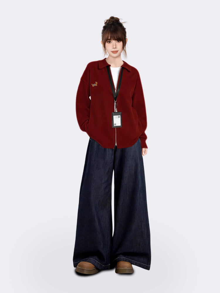 Full body shot of a woman wearing a red collared knit jacket and wide-leg denim pants.