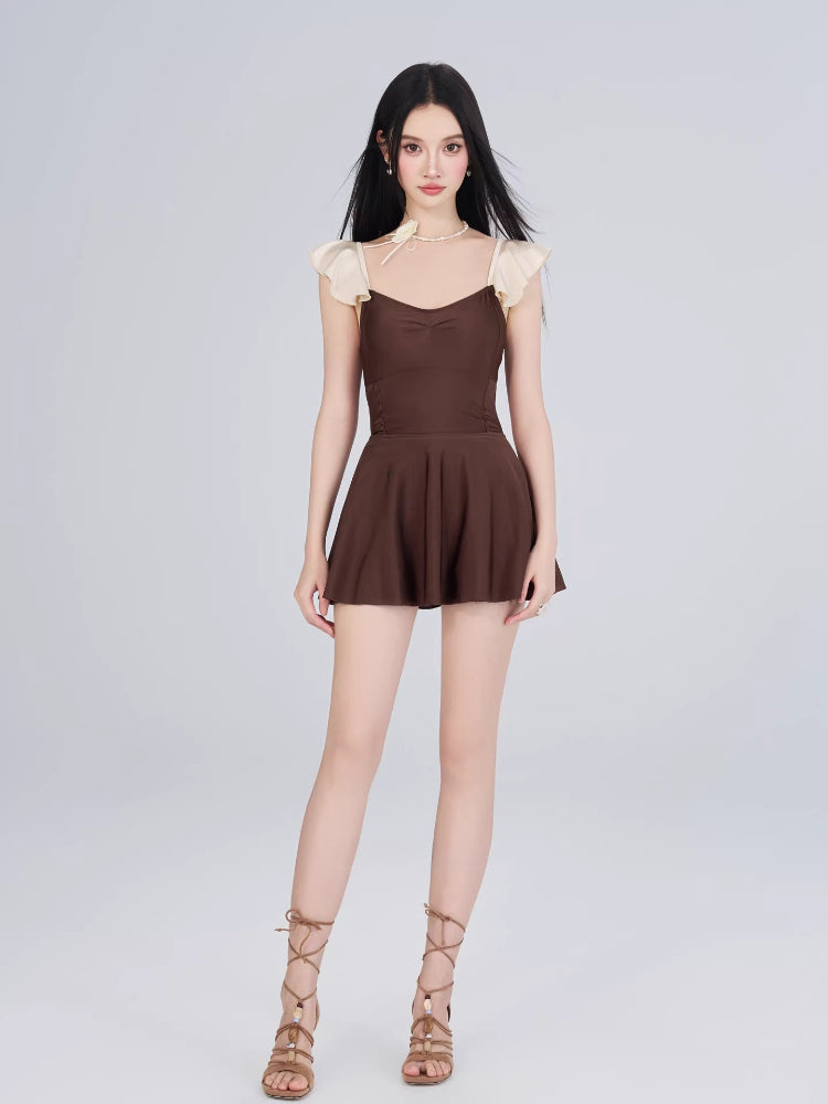 Woman wearing a brown and cream one-piece swimsuit with flutter sleeves and a skirted bottom.