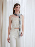 Model posing with hands in pockets, wearing a white lace camisole and cream trousers, with a striped knit scarf.