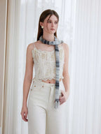 Model posing with hands in pockets, wearing a white lace camisole and cream trousers, with a striped knit scarf.