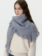Woman wearing a grey knit scarf with fringe detail over a cream sweater.