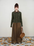 Full body shot of a woman in a dark green cable knit cardigan and brown wide-leg trousers.