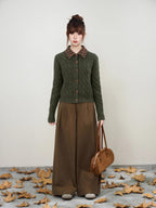 Full body shot of a woman in a dark green cable knit cardigan and brown wide-leg trousers.
