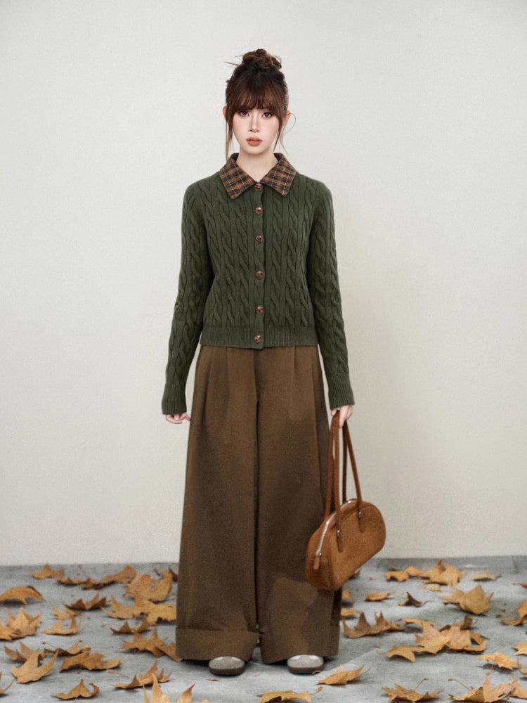 Full body shot of a woman in a dark green cable knit cardigan and brown wide-leg trousers.