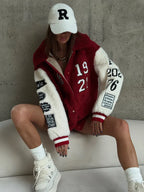Woman in a white baseball cap and a red and white sherpa fleece bomber jacket, showcasing embroidered patches on the sleeves.