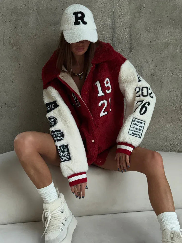 Woman in a white baseball cap and a red and white sherpa fleece bomber jacket, showcasing embroidered patches on the sleeves.