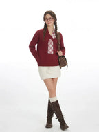 Model posing in a burgundy knit sweater with a plaid detail and a white skirt.