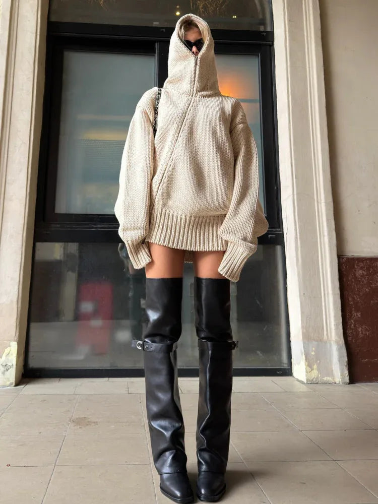 Woman posing outdoors in a beige hooded knit sweater and black leather boots.