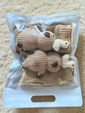 A pair of beige knitted ankle socks with sheep and duck appliques are laid out on a fluffy rug.