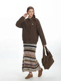 Full body shot of a woman in a brown bomber jacket, striped skirt, and brown shoes