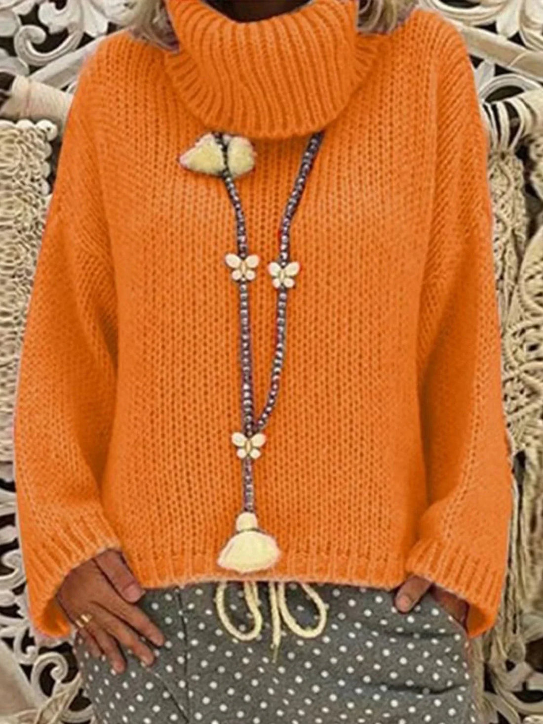 Woman wearing an orange chunky knit turtleneck sweater with a detailed beaded necklace featuring butterfly charms.