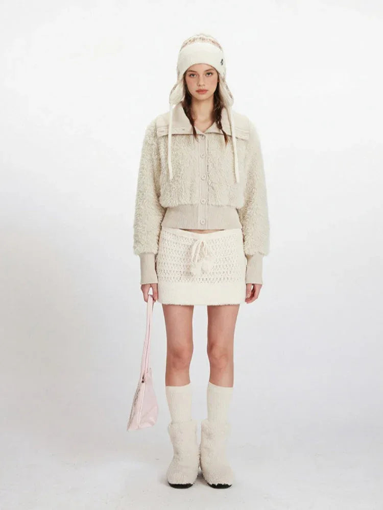 Woman wearing a cream fuzzy cropped jacket and matching mini skirt, with a knitted hat and boots