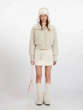 Woman wearing a cream fuzzy cropped jacket and matching mini skirt, with a knitted hat and boots