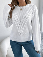 Woman wearing a white long-sleeve knit sweater with a V-shaped open-knit detail and blue jeans