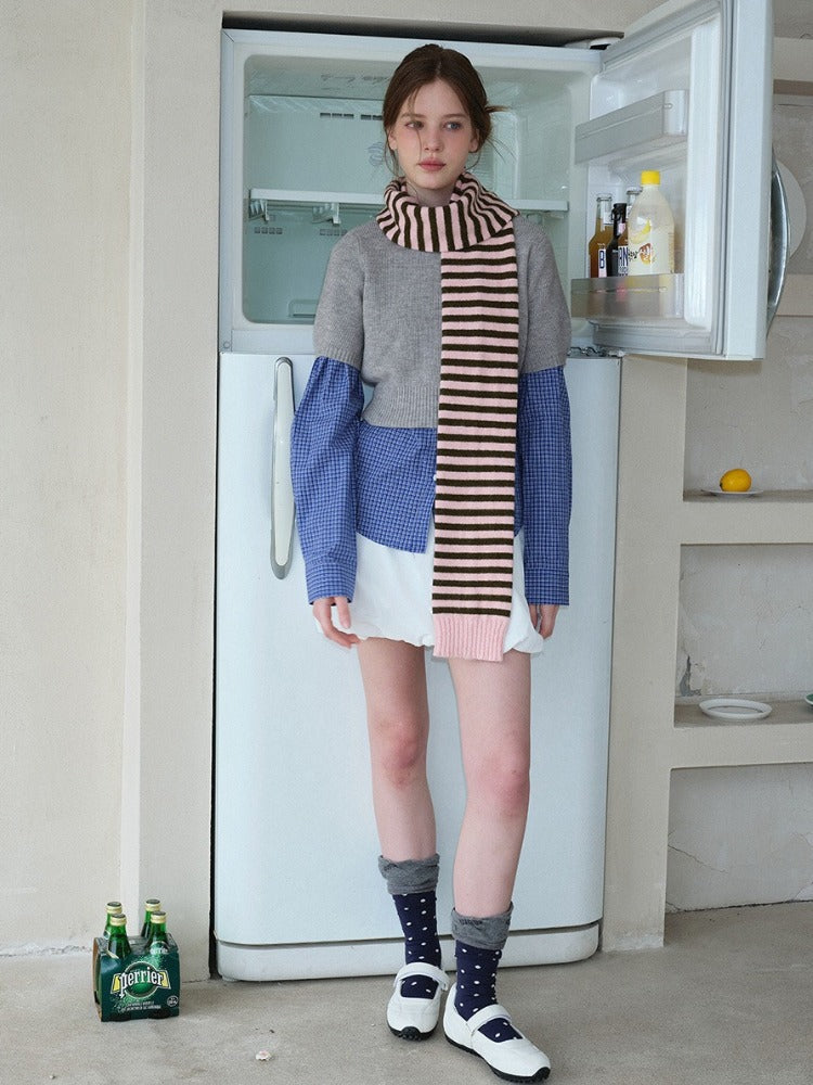 Woman wearing a grey cropped sweater over a blue gingham shirt, white bubble shorts, navy polka dot socks, white Mary Jane shoes, and a pink and brown striped scarf.