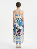 Back view of a woman wearing a white midi dress with an abstract botanical print and spaghetti straps, standing against a white background.