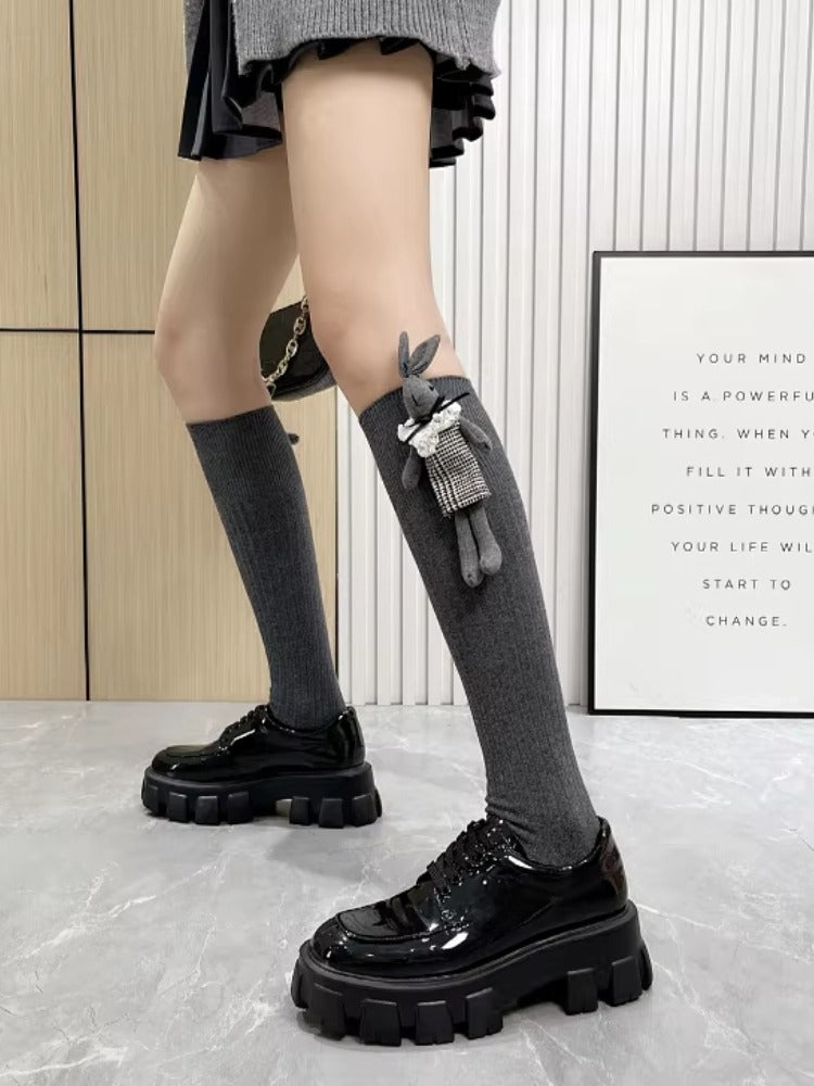 Full-length view of grey ribbed knee-high socks with a plush bunny charm, paired with a grey skirt and black platform shoes.