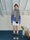Woman wearing a grey cropped sweater over a blue gingham shirt, white bubble shorts, navy polka dot socks, white Mary Jane shoes, and a black and white striped scarf.