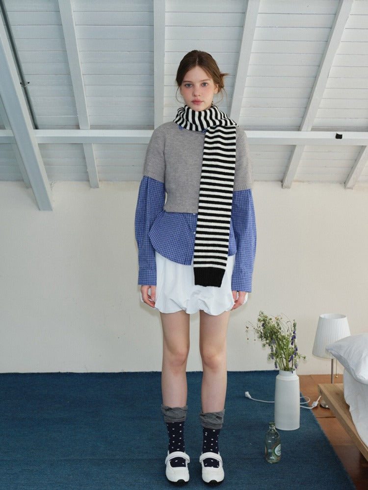 Woman wearing a grey cropped sweater over a blue gingham shirt, white bubble shorts, navy polka dot socks, white Mary Jane shoes, and a black and white striped scarf.