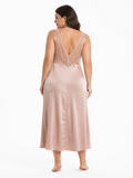 Back view of a plus size model in a blush pink satin midi slip dress featuring a deep V-neck lace back.