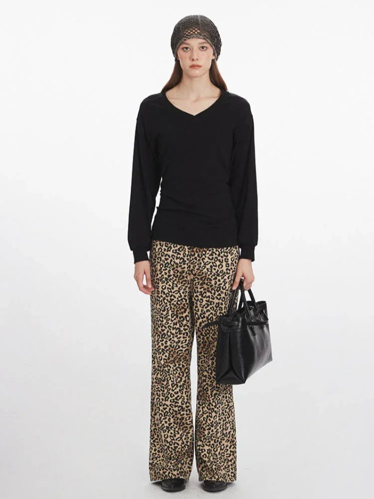 Model wearing a black V-neck long-sleeve top and leopard print wide-leg pants, holding a black handbag.