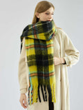 woman from the side, wearing a grey ribbed sweater and dark pants, with a long plaid scarf hanging down her front